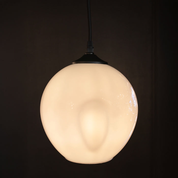 A spherical frosted glass pendant light glowing with a warm cream-white light, suspended by a black cord against a very dark, near-black background.