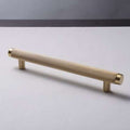 A gold-colored brass handle lying on a flat surface with a plain background.