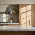 Modern kitchen with marble countertop, wooden cabinets, and silver nickel pendant light.