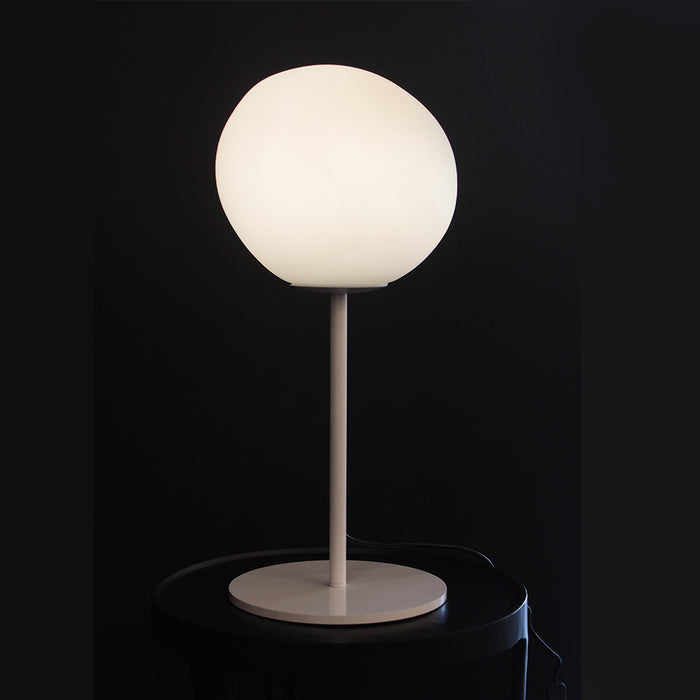 A modern table lamp with a large, rounded white globe shade on a slim matching stem and circular base, shown illuminated against a dark background.
