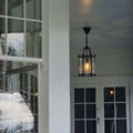 A black metal lantern-style pendant light with clear glass panels hangs from a ceiling on a porch with white-framed windows and doors.