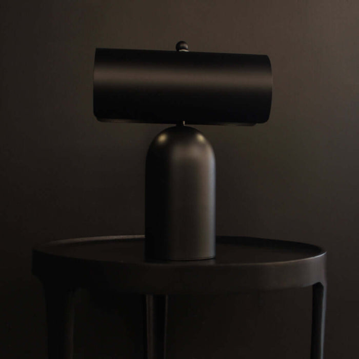 Forma Rechargeable Table Lamp on a black table, featuring a sleek matte black finish and touch-activated design.