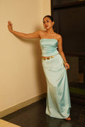 Woman in a light blue dress with gold accents posing against a plain wall.