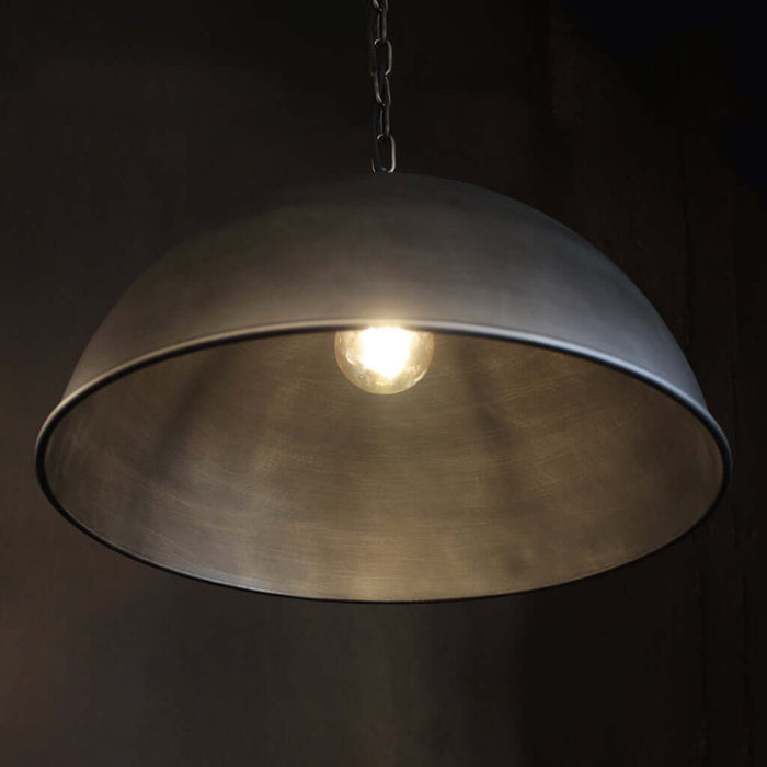 A dome-shaped pendant light with a brushed metal finish, suspended from a chain, with a glowing bulb visible inside against a dark background.