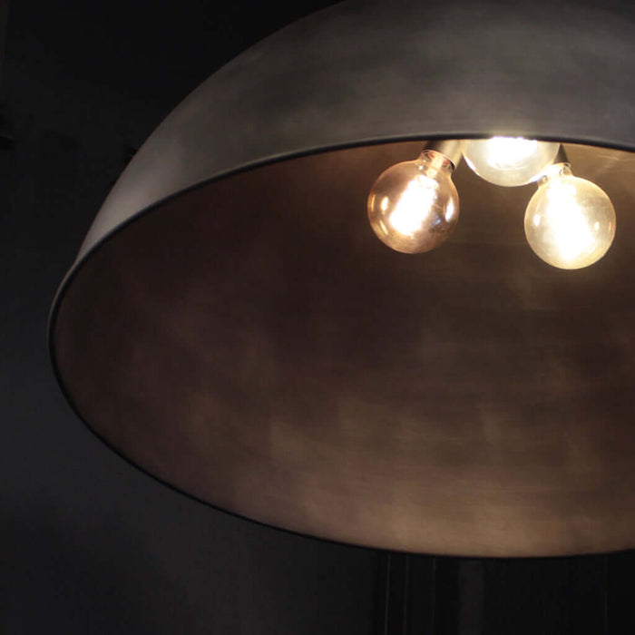 A close-up of a dome-shaped pendant light fixture with a dark silver metallic finish and three glowing warm Edison-style bulbs visible inside.