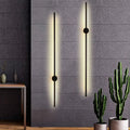 Contemporary wall lights with a matte black finish installed on a grey wall, with one light emitting a warm white glow.