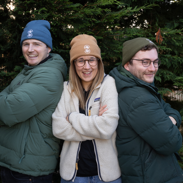 Three people standing together outdoors with trees in the background